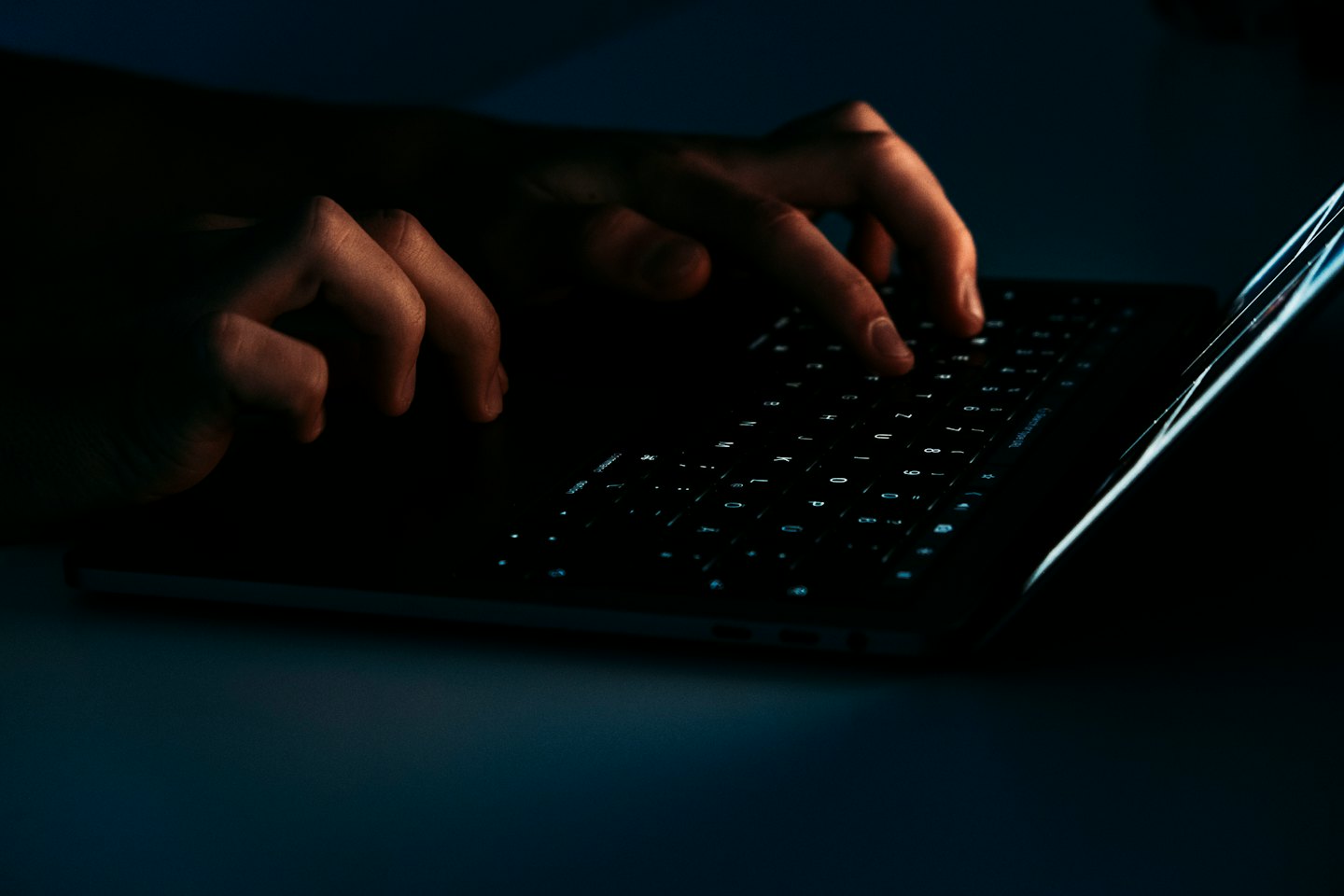 Händer som skriver på ett lysande laptop-tangentbord i mörkret.